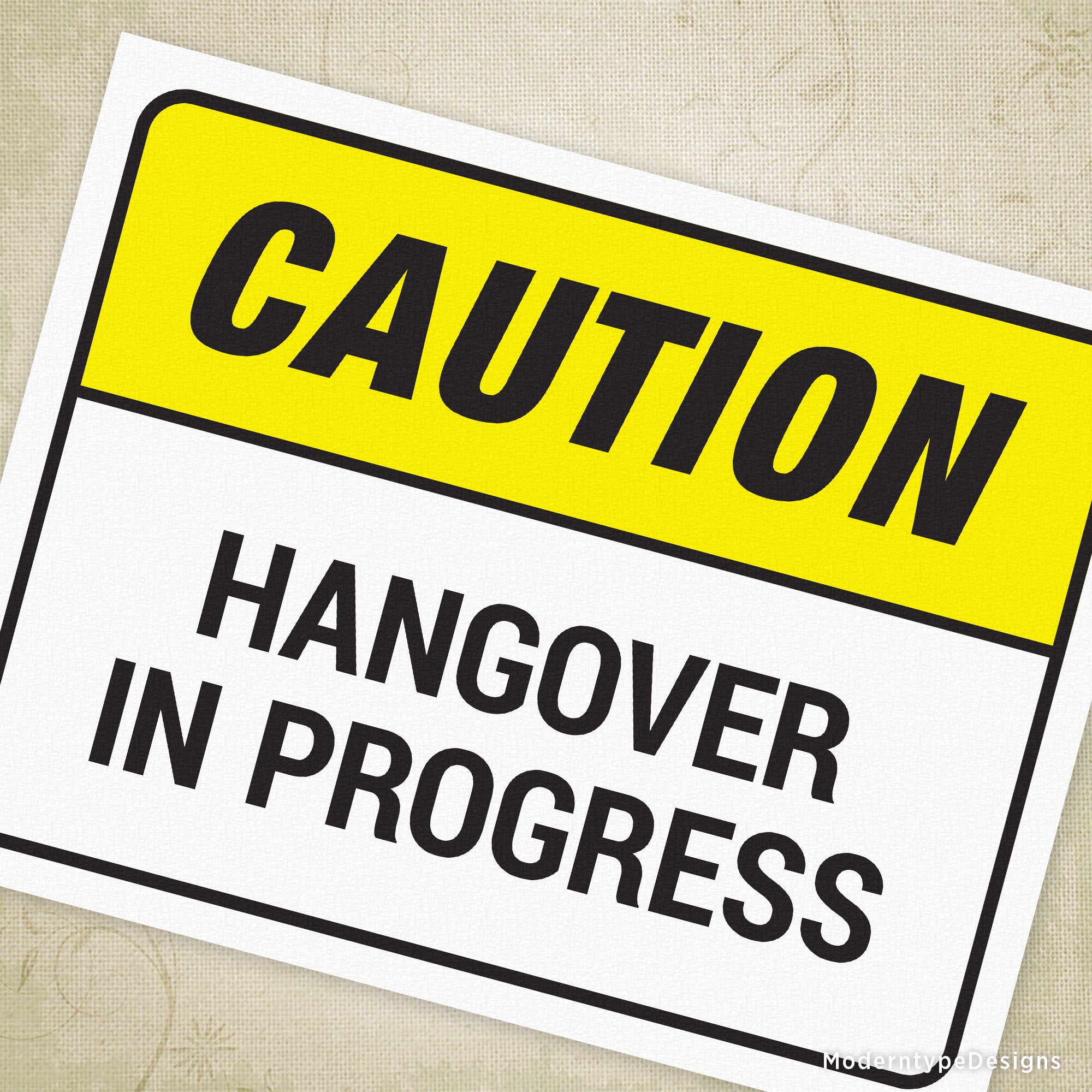 A printable sign with a yellow background and black text that reads 'CAUTION HANGover in PROGRESS' and a smaller text below that says 'This is a humorous sign and not a real warning.'.