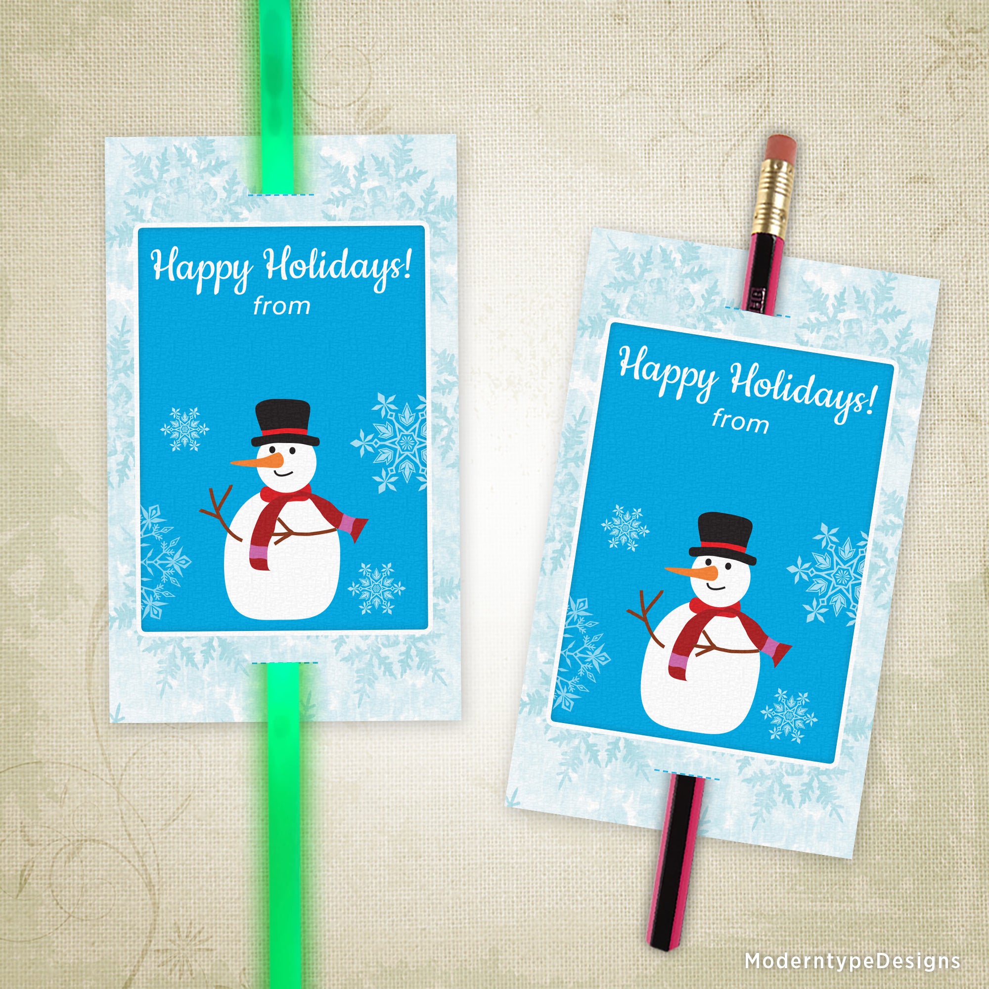 A printable holiday glow stick with a blue background featuring a cartoon snowman, snowflakes, and the text 'Happy Holidays from' along with a space for custom text entry.